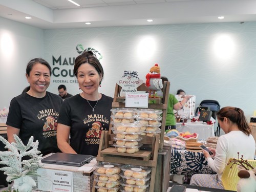 Women standing with table with pastries on it.