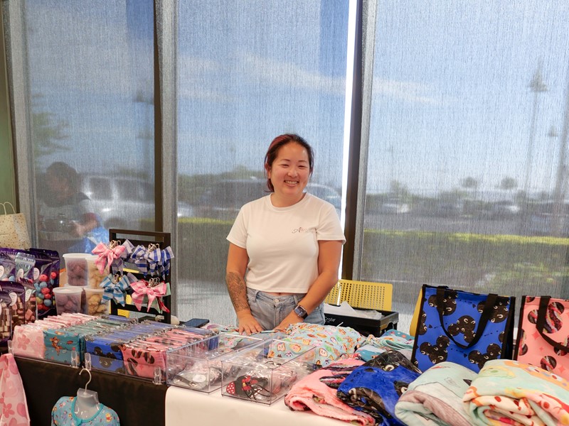 Woman standing behind table with clothes on it.