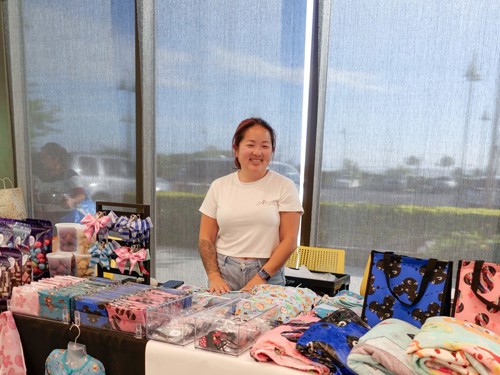 Woman standing behind table with clothes on it.
